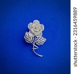 Small photo of Silver filigree brooch with stem and leaf floral pattern on blue background.