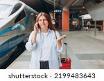 Small photo of Upset woman talking over phone disappointed hear bad news, sad pensive girl speaking having unpleasant phone conversation and standing at railroad station platform. Travel by train. Negative emotion