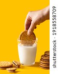 Small photo of Breakfast concept. Hand dipping sandwich biscuits cookie filling with chocolate cream anto a glass with milk on yellow background