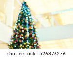 Blurred big bright Christmas tree decorated with colorful garlands and balloons in the lobby of shopping center. Bokeh basic background for design                               