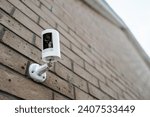 Small photo of Shallow focus of a wireless smart CCTV night and day camera seen after a heavy downpour on a house exterior wall. The blue motion LED indicator is seen active, showing its recording.