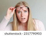 Shocked angry young woman in disbelief lowering glasses looking at camera with indignation isolated on grey blank studio background