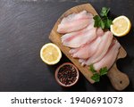 fresh fish fillet of tilapia with ingredients for cooking on wooden board, top view