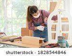 A confident young female carpenter uses a hand drill to assemble the wood window in the carpentry shop. Asian handywoman apprentice working in a workshop. DIY woodworking crafts and Hobbies concepts.
