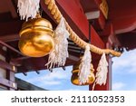 Shiny golden big suzu bells hung on a shimenawa rice or wheat straw rope adorned with suspended streamers known as shide and made with Japanese washi paper symbol of purity in a Shinto shrine.