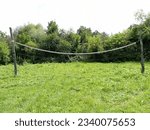 An improvised volleyball court on a green grass lawn with a poorly stretched net between two wooden posts