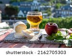 Products of Normandy, cow neufchatel lait cru cheese and glass of apple cider drink with view on houses of Etretat village on background, Normandy, France