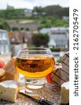 Small photo of Cow cheeses of Normandy region - camembert, livarot, neufchatel, pont l'eveque and glass of apple cider drink with houses of Etretat village on background, Normandy, France