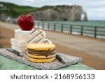 Small photo of Cheeses of Normandy served outdoor, round camembert cow cheese, yellow livarot, heartshaped neufchatel and view on alebaster cliffs Porte d'Aval in Etretat, Normandy, France