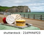 Small photo of Four famous cheeses of Normandy, pont l'eveque, round camembert cow cheese, yellow livarot, heartshaped neufchatel and view on promenade and alebaster cliffs Porte d'Aval in Etretat, Normandy, France
