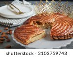 Small photo of A piece of traditional French galette des rois with golden crown, almonds plate and cutlery. Cake made with puff pastry and creamy paste filling roll in circle shape. It's usually served on Epiphany