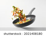 Fresh vegetables fly in a pan on a white background. Cooking with various chopped vegetables in a pan. The concept of healthy eating and diet. 