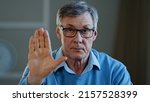Small photo of Serious old senior mature 60s man stretch out palm to camera says stop gesture indoors. Social problems older generation disrespect ban refusal disagreement. Aged businessman trouble denial rejection