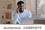 Small photo of African american man businessman freelancer worker talk chatter on mobile cellphone with client make business call discussion listen news explain information looks at laptop screen use gadget