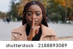 Small photo of Close-up young confident mysterious african american woman standing outdoors showing silence gesture puts finger to mouth forbids speaking prohibits disclosure confidential information secret