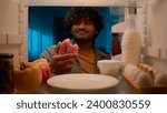 Small photo of Point of view POV from inside refrigerator hungry Indian man Arabian guy male at night kitchen open fridge want eat take bitten sweet donut smiling condemn bakery unhealthy food nutrition overeating