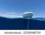 Small photo of luxury boat sitting on anchor floating in deep blue water with blue sunny skies in background. Split shot of the bow and anchor line of luxury boat as it floats in the ocean in the Bahamas.
