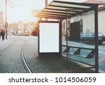 Glass and metal tram stop with railway track near and blank white mock-up of informational banner inside; empty advertising billboard placeholder stand in urban settings next to tramway and city road