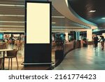 An empty vertical advertising banner mockup in front of a crowded shopping mall or an airport food court with tables and customers in the background and a copy space place on the right for an ad text