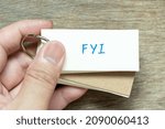 Small photo of Man hold the flash card with handwriting word FYI (Abbreviation of For your information) on wood background