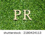 Small photo of Wood alphabet letter in word PR (Abbreviation of purchase requisition or public relations) on green grass background