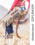 Small photo of detail photo of cowgirl wearing chinks on horseback