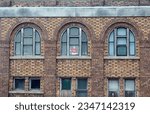 Small photo of Santa Claus doll in arched window. Old brick building. Summer. Months until Christmas. Incongruity. Incongruous. Santa looking out overseeing things. Funny. Humor.