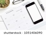 Top view of smart phone isolated white screen for mockup design or app display with calendar, eyeglasses and pen on white wooden background
