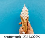 Ice cream cone on a blue background. The woman holding the ice cream by hand.
