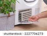 Small photo of Drying machine with a full filter of lint, hair, dust, wool after the drying cycle of towels, bed linen. White drying machine. A man takes out a dirty radiator dryer. tumble dryer