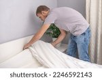 Small photo of A man makes his cozy bed with fresh bright white bed linen. Making the bed with fresh bed linen by a white man. The day of the change of bedclothes. The day of washing bedclothes in the laundry room.