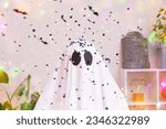 Small photo of White ghost costume for Halloween party with neon lights in the background. The ghost is celebrating Halloween. A ghost at a confetti party. Portrait of a ghost. The monster is celebrating Halloween.