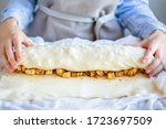Hands wrap the dough with apple filling make apple strudel.Girl is preparing a pie at home in an apron.Work with puff pastry.The process of making apple strudel.Mom makes a pie.Apple strudel roll.