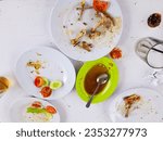 Small photo of Leftover plates, glasses, spoons, leftover vegetables, chili sauce, sweet iced tea and leftover chicken bones. On a white table.