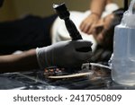 Small photo of Photograph of a tattoo machine grabbing ink with its needle next to Vaseline in a tattoo studio during a session for a female client