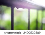 Small photo of Blurred image of wet iron railing with water drops after rain in the afternoon. Black iron railing. water drops on black gate. scenery light after rain on black railing. background concept copy space