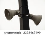 two beige train station speakers pointing in opposite directions fastened to a black rectangular post outside at train station with sky in background