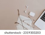 Small photo of Stylish office workspace desk. Wireless earphones, glasses, laptop, envelopes on tan beige table. Aesthetic neutral tan beige and white colours.