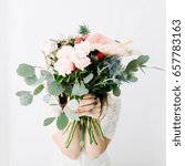 Small photo of Pretty woman with beautiful flowers bouquet: bombastic roses, blue eringium, anthurium flower, eucalyptus branches at white wall. Front view. Floral lifestyle composition.