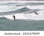 Small photo of SENNEN COVE, CORNWALL, ENGLAND - 22 OCTOBER 2014: Surfers catching a wave on a cold autumn day, on 22 October 2014 in Sennen Cove cornwall England.