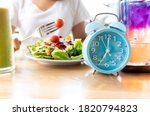 Selective focus of blue clock which woman make a Intermittent fasting with  a Healthy food of salad .Healthy lifestyle Concept.
