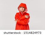 Blond girl in a red raincoat with a hood standing isolated over white background. Are you ready for cold bad weather?