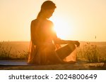 Beautiful girl sit in yoga lotus pose against sun in warm light, wear transparent cloth, meditation and stretching outdoors