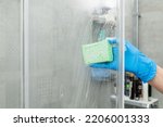 Woman in a blue glove cleans a shower cabin from limestone