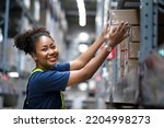 Small photo of African American warehouse worker take flat box from shelf in big warehouse factory, Online shopping store for logistic service to deliver the shipment, check barcode before passing to transportation