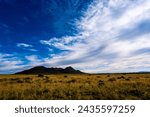 Small photo of Golden grassy frontage and a small well defined hill and a backdrop of deep blue sky with a sweep of white cloud covering more than half the sky