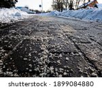 Salt grains on icy sidewalk surface in the winter. Applying salt to keep roads clear and people safe in winter weather from ice or snow, closeup view.