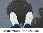 Person in gray boots standing on pavement wet after rain, top view. Close-up of legs in shoes, pov.