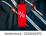 Sale, black friday concept. Red tag with Percentage discount sign and text Black Friday hanging on dark blue jacket in clothing store, close-up.