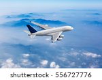 White passenger plane in the blue sky. Aircraft flies high over the clouds and foggy mountain landscape. Airplane side view.